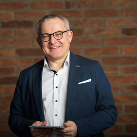 Martin Rotter mit einem Tablet in der Hand vor einer Ziegelmuauer.