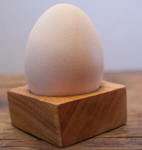 Hühnerei in Eierbecher aus Kirschholz auf Holztisch.
