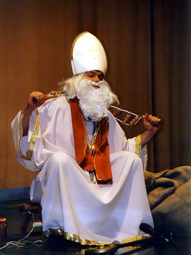 Nikolaus sitzt auf der Bühne und massiert sich mit einem Massagegerät