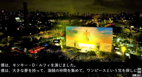 主演俳優のインタビューの日本語字幕表示の様子。たくさんの観客と巨大なスクリーン、ステージにはワンピースのルフィを演じた俳優さんが登壇してスピーチしている様子の映像と、その下に字幕が表示された写真です。