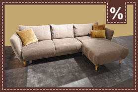 Beigefarbenes Ecksofa im modernen Stil mit drei goldgelben Kissen. Prozentzeichen in der Ecke.
