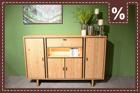 Helles Highboard in Holzoptik mit schwarzen Absetzungen, einem Fach, einer Schublade und 4 Schranktüren vor einer grüner Wand