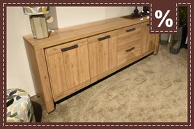 Sideboard in Holzoptik und schwarzen Metallgriffen. Daneben steht ein Hocker 