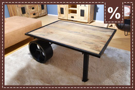Rustikaler Couchtisch aus Holz mit schwarzem Metallrahmen und einem großen Rad als Bein. Prozentzeichen.
