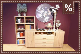 Sideboard aus hellem Holz mit offenem Regal und Deko vor einer dunkellilaen Wand. Prozentzeichen.