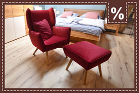 Roter Sessel und Fußhocker, darauf ein rotes Kissen vor einem Bett 