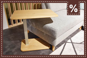 Kleiner, rechteckiger Beistelltisch mit Holzplatte auf einem grauen Sofa. Prozentzeichen.