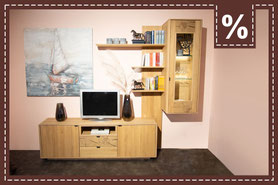 Wohnwand aus hellem Holz mit Vitrine vor rosafarbener Wand. Prozentzeichen in der Ecke.