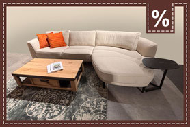 Beigefarbenes Ecksofa mit orangefarbenen Kissen und Couchtisch aus Holz. Prozentzeichen.