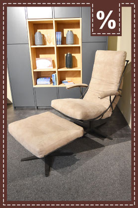 Sessel mit Fußhocker in creme vor einem dunkelgrauen Schrank