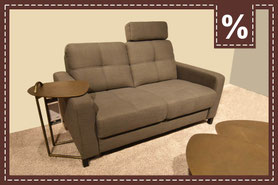 Graues Zweisitzer-Sofa mit verstellbarer Kopfstütze und Beistelltisch. Prozentzeichen in der Ecke.