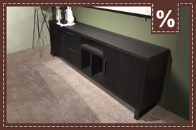 schwarzes Sideboard mit 3 Fächern, 2 Schranktüren und 2 Schubladen auf einem hellgrauen Teppich und vor einer grünen Wand