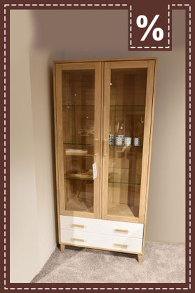 Hohe Vitrine aus Holz mit Glastüren und zwei Schubladen mit weißen Fronten. Prozentzeichen.