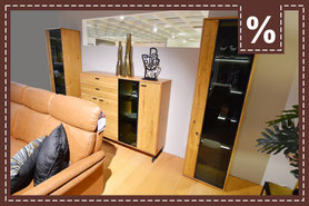 Wohnzimmermöbel aus hellem Holz mit Vitrinen, Sideboard und braunem Ledersofa. Prozentzeichen.
