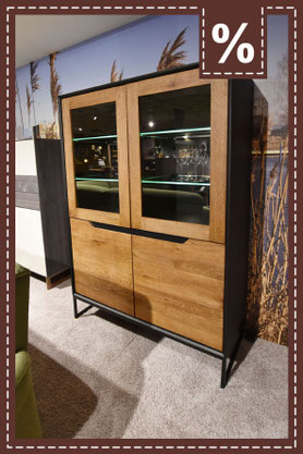  Eine moderne Vitrine in Holzoptik mit Glastüren, beleuchteten Fächern und schwarzem Rahmen. Prozentzeichen in der Ecke.