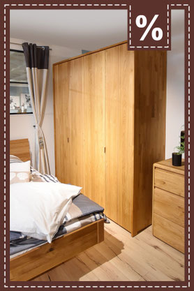  Ein hoher, sechsteiliger Kleiderschrank aus hellem Holz im Schlafzimmer. Prozentzeichen in der Ecke.