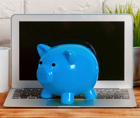 Laptop vor einer weißen Wand mit einem blauen Sparschwein