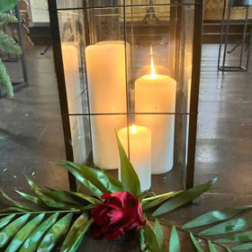 Nahaufnahme einer großen Laterne mit mehreren brennenden weißen Stumpenkerzen auf dem Boden der Kapelle auf dem Bergfriedhof Sankt Andreasberg. 