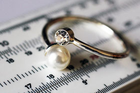 Ein Goldring mit einer Perle, der auf einem Maßband eines Juweliers liegt.