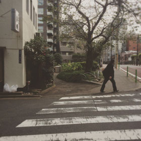 公園の端まで来て頂くと交差点にさしかかります。左手の天ぷら屋さんと写真中央の大きな木の間の小道にお進みください。