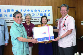 本間支所長(右)が「ゆうパック箱八重山版」を漢那副市長に贈呈した=20日、市役所庁議室