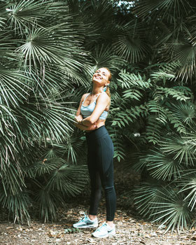 Glückliche, strahlende und junge Frau trägt Yoga Trainingskleidung im Grünen. Gute Körperhaltung mit Feel the Flow, Bern. Angelos Michalopoulos