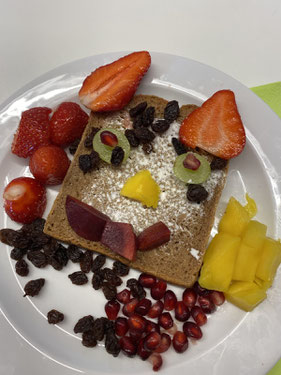 Gesundes Brotgesicht: Brot mit Frischkäse, Erdbeeren, Trauben, Paprika, roter Beete und Granatapfelkernen sowie Rosinen