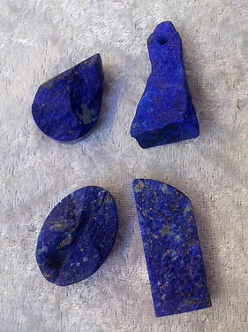 Auf weißem Samttuch liegen 4 Stücke dunkelblaue Lapislazuli in verschiedenen Formen.