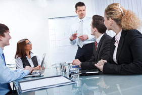 Ein Meeting mit fünf Personen in Anzügen an einem Glastisch