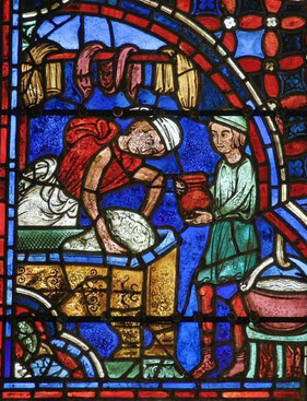 Un boulanger pétrit la pâte, dans laquelle on distingue le visage du Christ. Vitrail de Chartres. Baie des Apôtres.