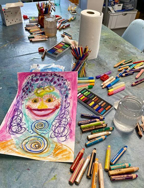 Maltisch im Atelier mit fröhlichem Bild einer Frau und bunten Stiften