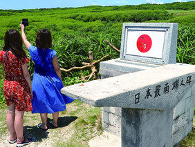 「日本最南端の碑」と「聖寿奉祝の碑」を背景に写真撮影する観光客。周辺は撮影スポットとなっている=20日、波照間島