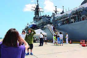 艦内見学を終えた後、ブースの制服を身に着け、護衛艦を背に写真を取る人は多かった。自衛官と一緒にわが子の写真を撮る親の姿もあった=2日、中城港湾の新港地区