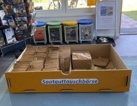In einer rechteckigen Schublade mit der Aufschrift "Saatguttauschbörse" sind kleine Tüten Saatgut alphabetisch sortiert.
