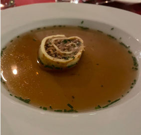 Ein tiefer weisser Teller, darin eine klare Wildkraftbrühe, in der Mitte ein Crêpe-Röllchen mit gehackten Waldpilzen