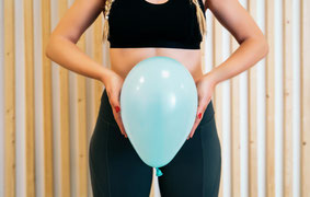 Frau die einen Luftballon vor ihren Bauch hält