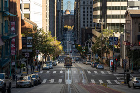 Blick die steile California Street hinunter auf die Skyline und eine vorbeifahrende Cable Car.