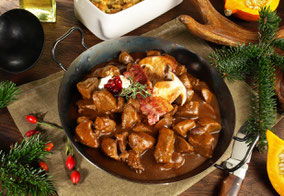 Gußpfanne mit zubereitetem Gulasch in dunkler Sauce mit einem Speckstreifen, Pilzen, Creme Fraîche-Klecks und Rosmarinzweig