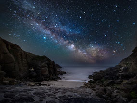 Sternenhimmel, der wie verzaubert wirkt über Felsen am Meer