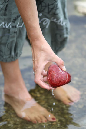 Susann mit Füßen im Wasser und herzförmigem Stein in der Hand