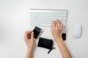 Un Clavier, une souris, un porte monnaie noir devant le clavier et deux mains dont une qui tapote dessus, et une qui tient une carte de crédit prête à proceder au paiement