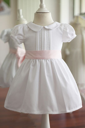 Robe cérémonie fille en piqué de coton blanc et dentelle de coton avec une ceinture rose. Modèle de robe Inès créé par Fil de Légende. Magasin vêtements cérémonie enfants Paris, Neuilly-sur-Seine. Expéditions en France et à l'International.