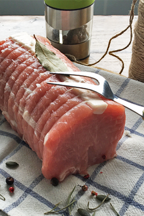 Rôti de porc frais prêt à cuire avec une feuille de laurier dessus, présenté sur un torchon à carreaux