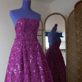 Sur l'image, une robe longue pour une occasion spéciale, bustier avec les épaules déshabillées et jupe longue et fluide. Réalisation par la maison de Couture Fil et Paillettes dans un tissu mauve en broderie relief de fleurs. 