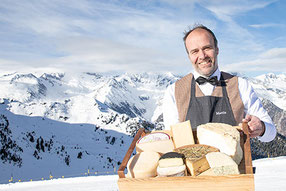 Käse-Sommelier mit Südtiroler Käseauswahl auf Holzbrett vor verschneiter Bergkulisse am Speikboden im Ahrntal.