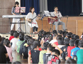 登野城小学校で平和集会が開催され、浦崎喬校長(右)は自作の曲を披露した=18日午前、同校体育館