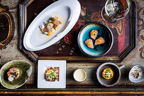 Kosterlemenü im Romantik Hotel Stafler: mehrere kleine Gourmetgerichte kunstvoll angerichtet auf einem rustikalen Holztisch, serviert als Degustationsmenü mit Weinbegleitung.