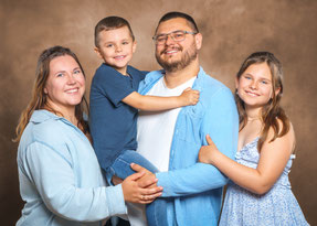 Familienfoto von Foto Schuh: Eine Familie steht zusammen im Fotostudio, lacht gemeinsam in die Kamera und trägt farblich abgestimmte Kleidung.