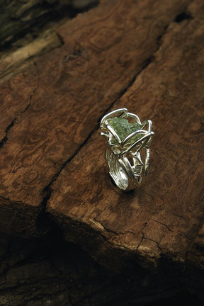 Bague en argent avec une pierre à cristaux verts qui repose sur du bois