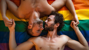 Two men holding each others hands, while lying on a pride flag